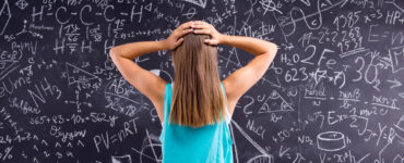 young woman standing hands on head confused in front of chalkboard full of math equations