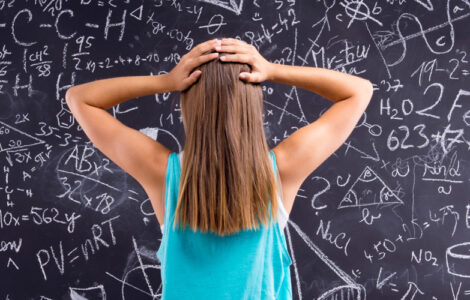 young woman standing hands on head confused in front of chalkboard full of math equations
