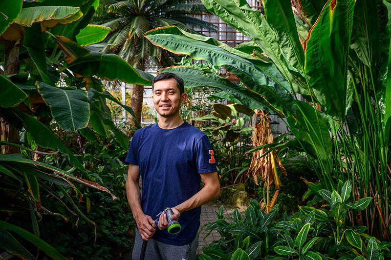 Illinois botany student in a greenhouse surrounded by plants