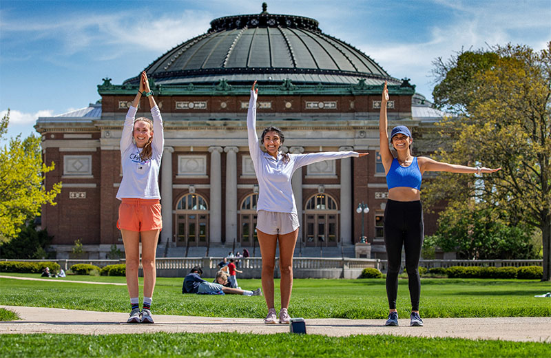 three students on the Quad posing, forming the letter I L L with their arms