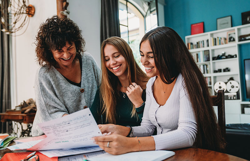 mother, daughter, and her friend looking through college applications in their home