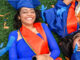 overhead of two smiling graduating students laying on the orange and blue confetti grass at Memorial Stadium