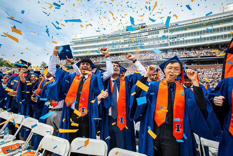 graduates celebrate graduation admist a flurry of orange and blue confetti on a beautiful day at Memorial Stadium