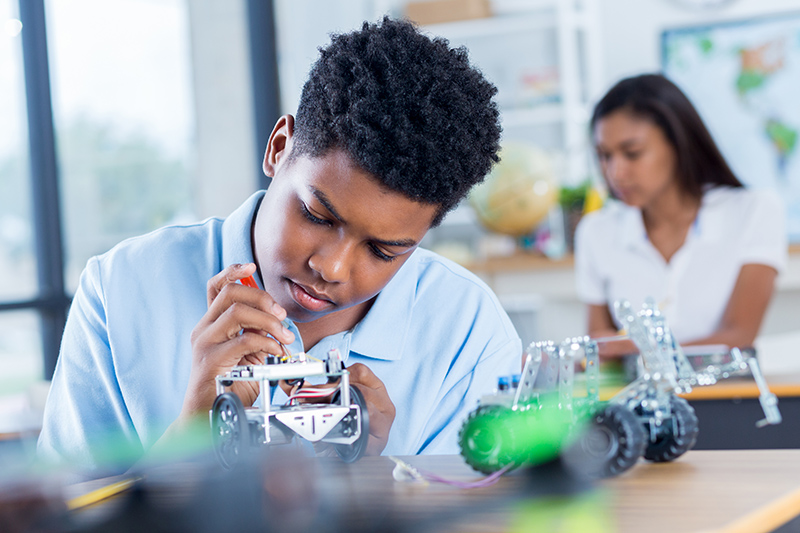 Teenage boy concentrates as he builds a robotic vehicle during engineering class.